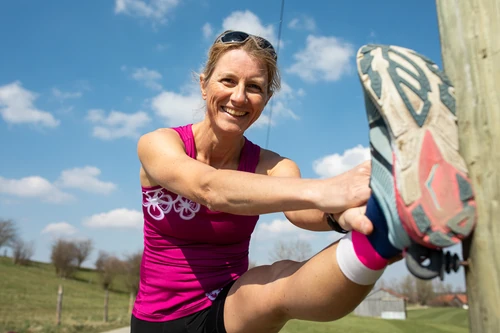 Petra Paule dehnt sich an einem Holzpfosten, den Laufschuh in Hüfthöhe