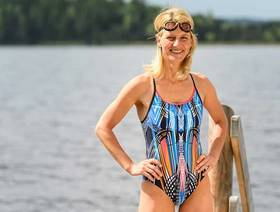 Petra Paule im Badeanzug auf einem Steg am See, Schwimmbrille auf der Stirn