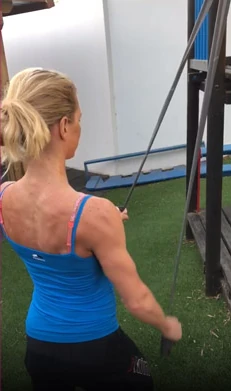 Petra Paule von hinten im blauen Trägertop, zieht im Garten an einem Zugband